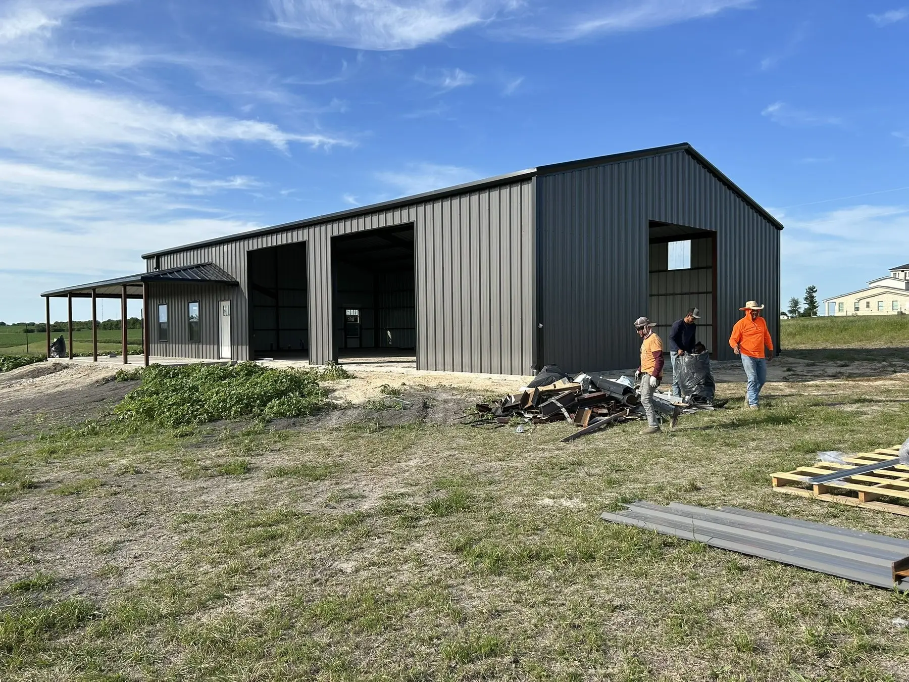 Charcoal barndominium, crew finishing trim — built by Rodriguez Metal Buildings, Central Texas